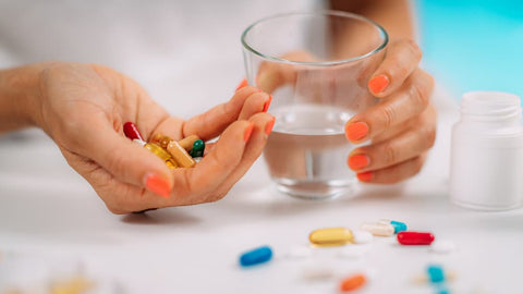 Femme tenant un verre d'eau et plusieurs pilules de couleurs différentes