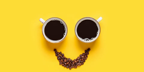 Deux tasses de cafés et des grains de cafés formant un visage sur un fond jaune