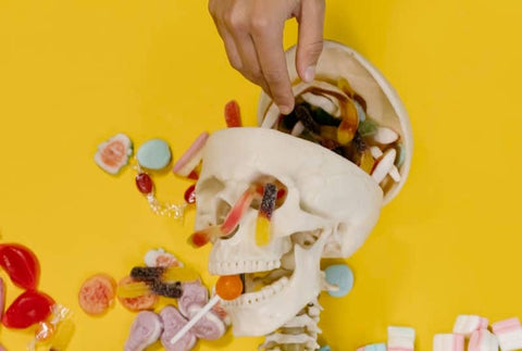 faux crâne rempli de bonbon avec une main qui pioche dedans sur fond jaune