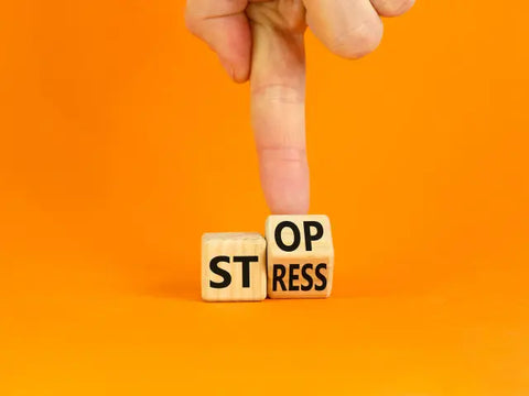 Stop stress écrit avec des petits cube en bois tenu par une main sur fond orange 